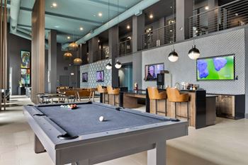 A pool table is in the middle of a room with a bar and television.